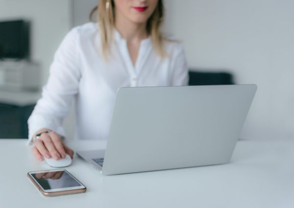 A woman working at a desk using a laptop and smartphone, exemplifying remote work.